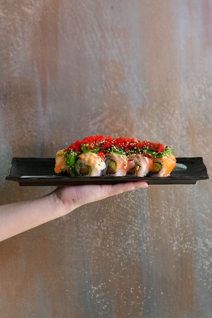 Roll mit rotem Tobiko auf einer Platte in der Hand serviert