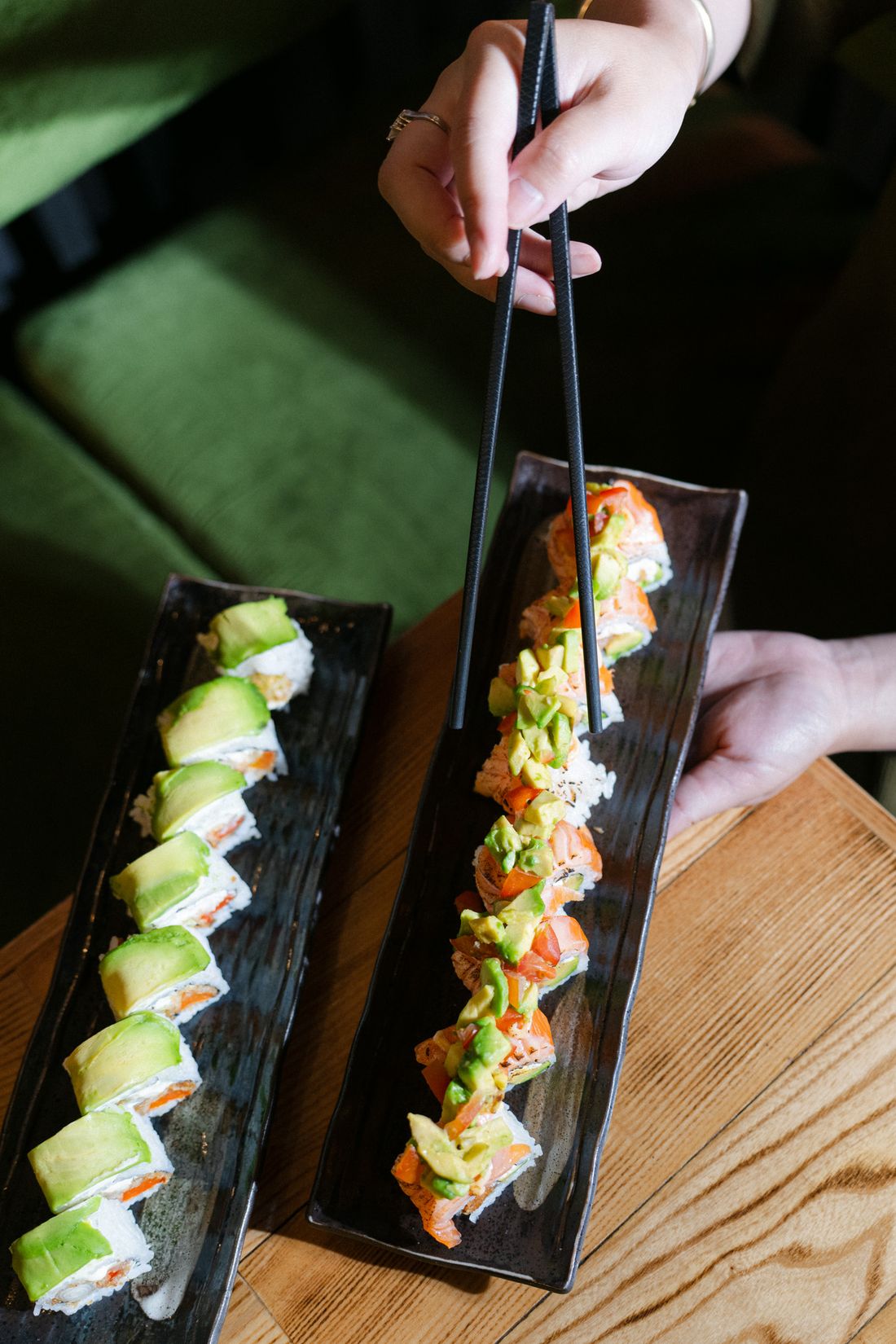 Zwei Sushi Platten mit Avocado Rolls, eine Rolle wird mit Stäbchen genommen